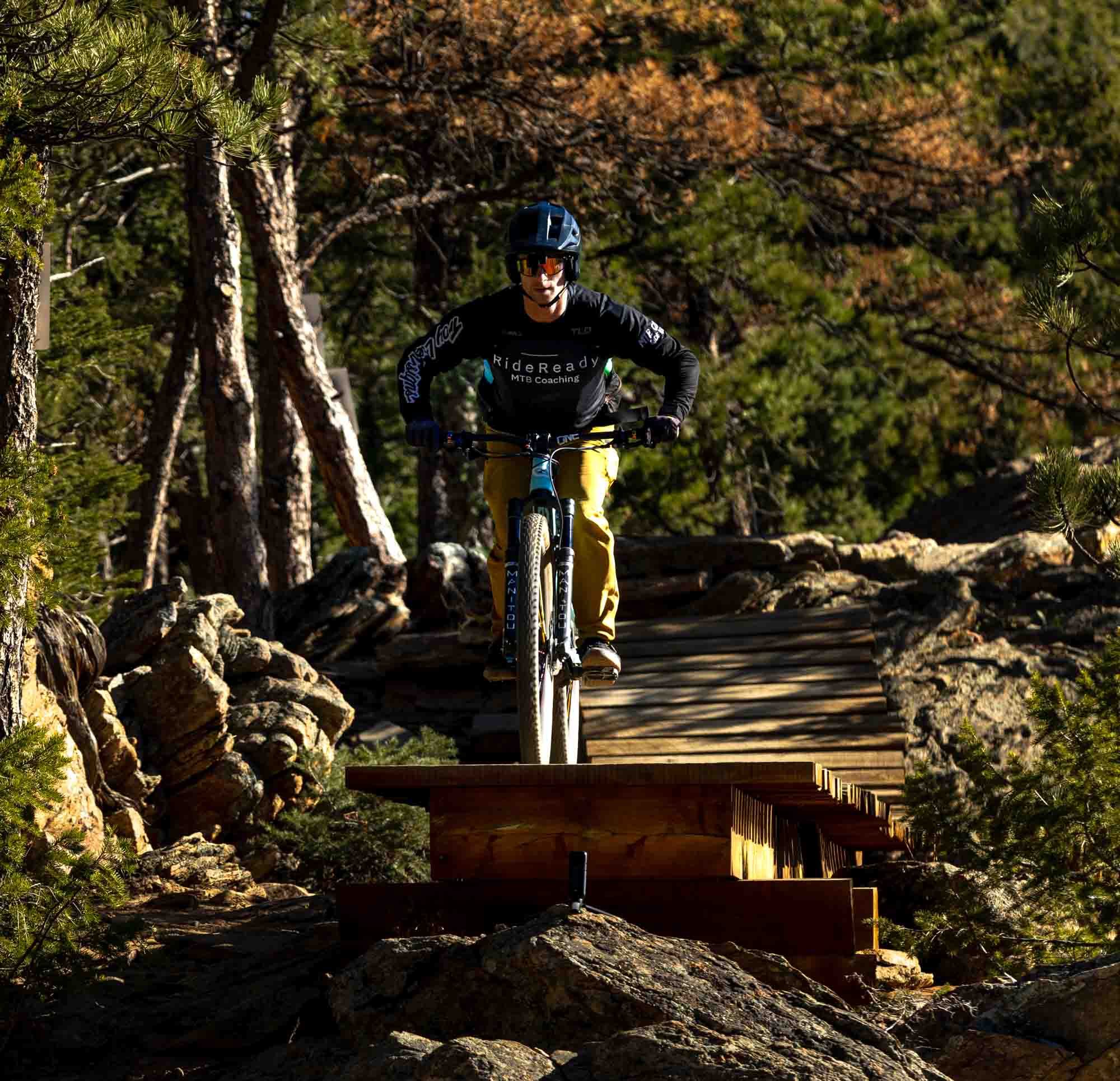 mountain biker riding wooden trail feature in forest filmed for mountain biking brand video production